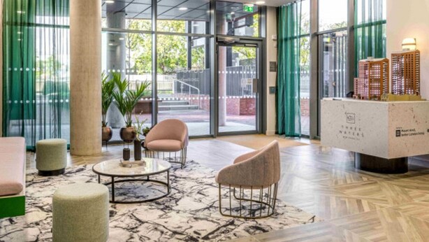 Een hal met een marmeren vloer, twee ronde tafels en twee stoelen. Er is een receptiebalie met een modelgebouw erop.