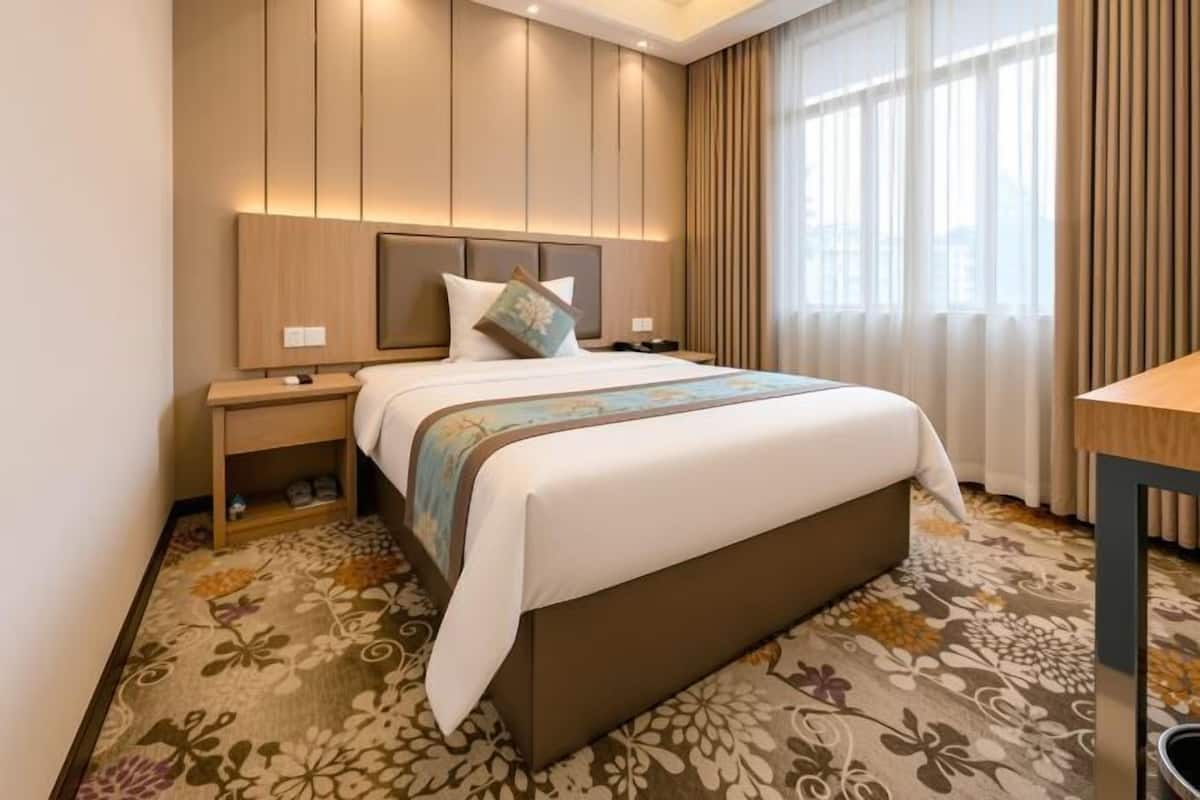 Habitació d'hotel amb un llit, una taula de nit, un escriptori i una finestra amb cortines.