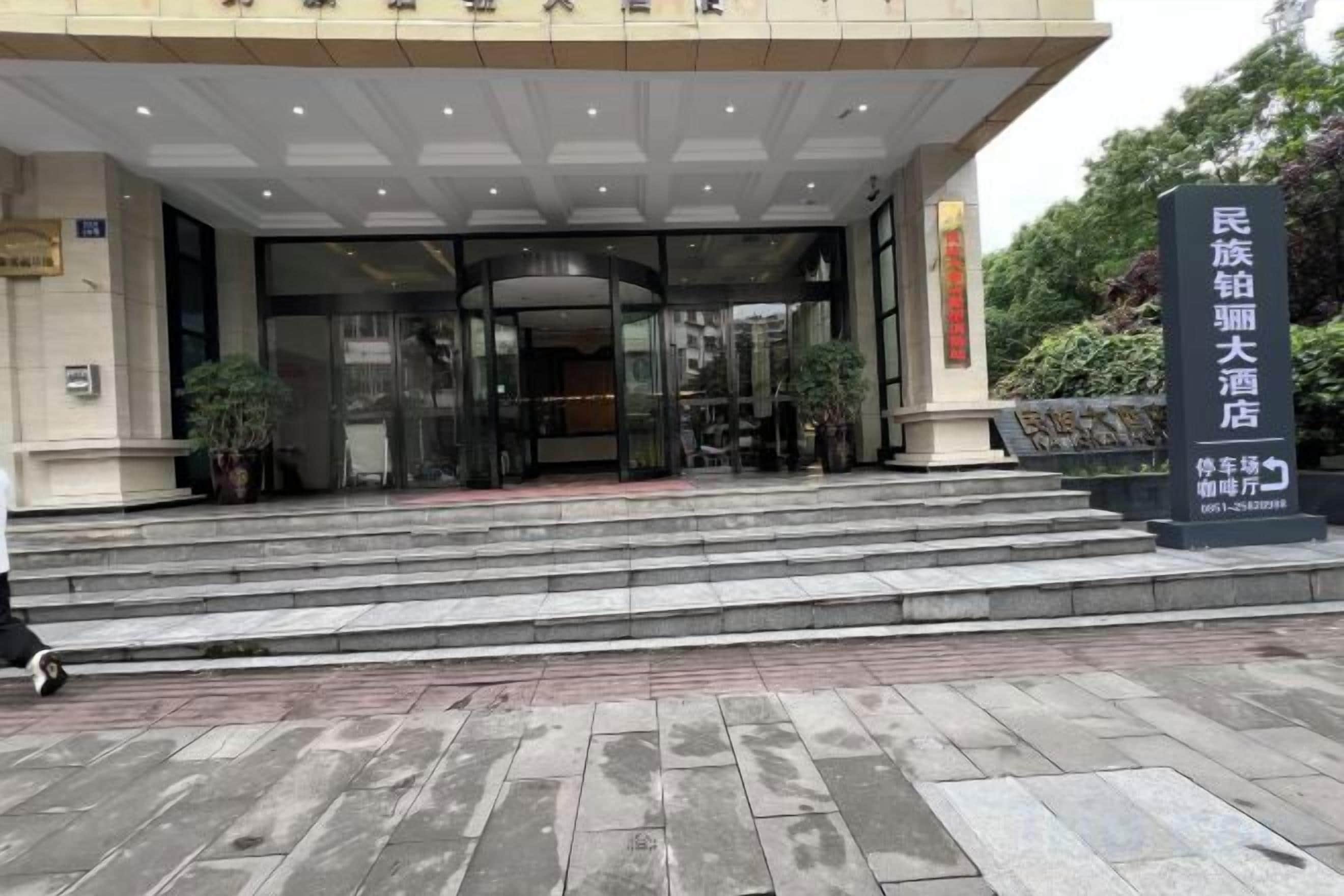 Entrada de un hotel con puerta de vidrio, escalones que conducen a ella y un letrero con caracteres chinos.
