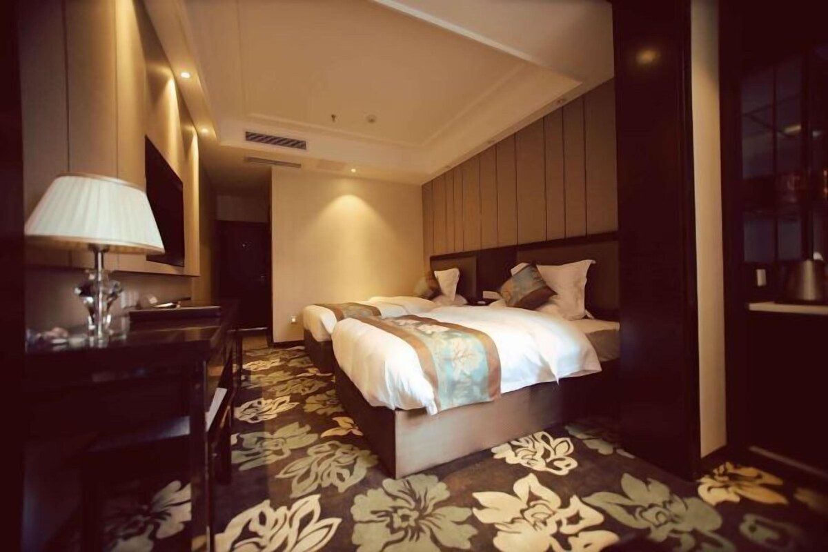 A hotel room with a bed, a desk with a lamp, and a large mirror.
