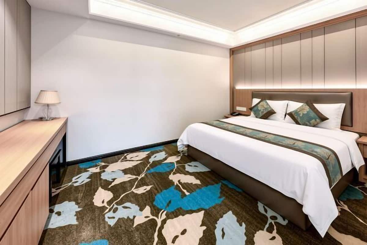Habitació d'hotel amb llit, taula de nit, làmpada i una catifes amb dibuixos.