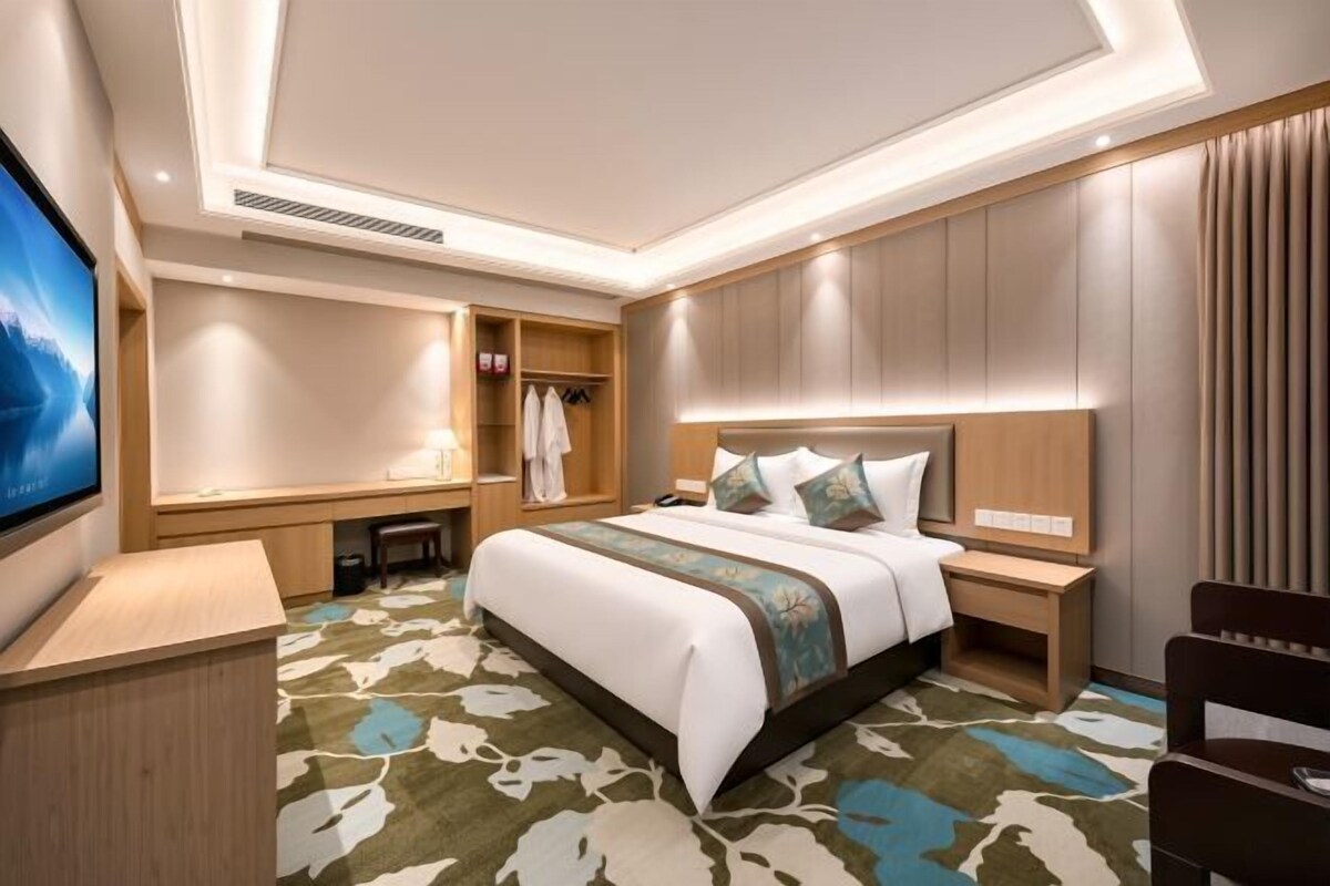 A hotel room with a bed, bedside tables, a desk, a TV, and a wardrobe.