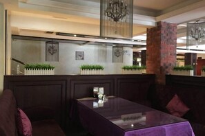 A restaurant with a high ceiling, chandeliers, and a brick column. There are cushioned seating areas and a table with a glass top. - National Hotel (Daozhen)