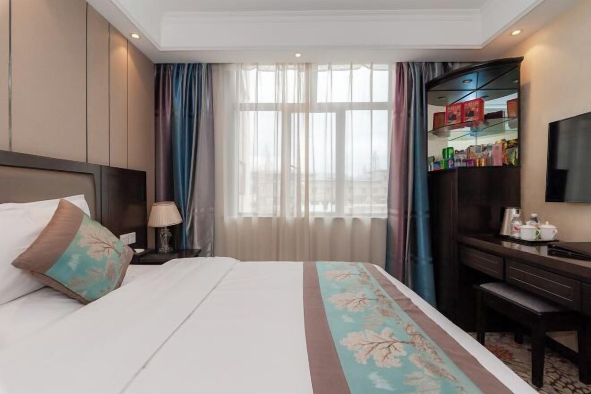 A hotel room with a bed, a desk, a wardrobe, and a television.