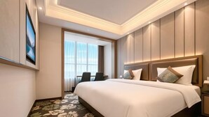 Ein Hotelzimmer mit einem großen Bett, einem Schreibtisch mit Stuhl, einem Fenster mit Vorhängen und einem am Wand montierten Fernseher.