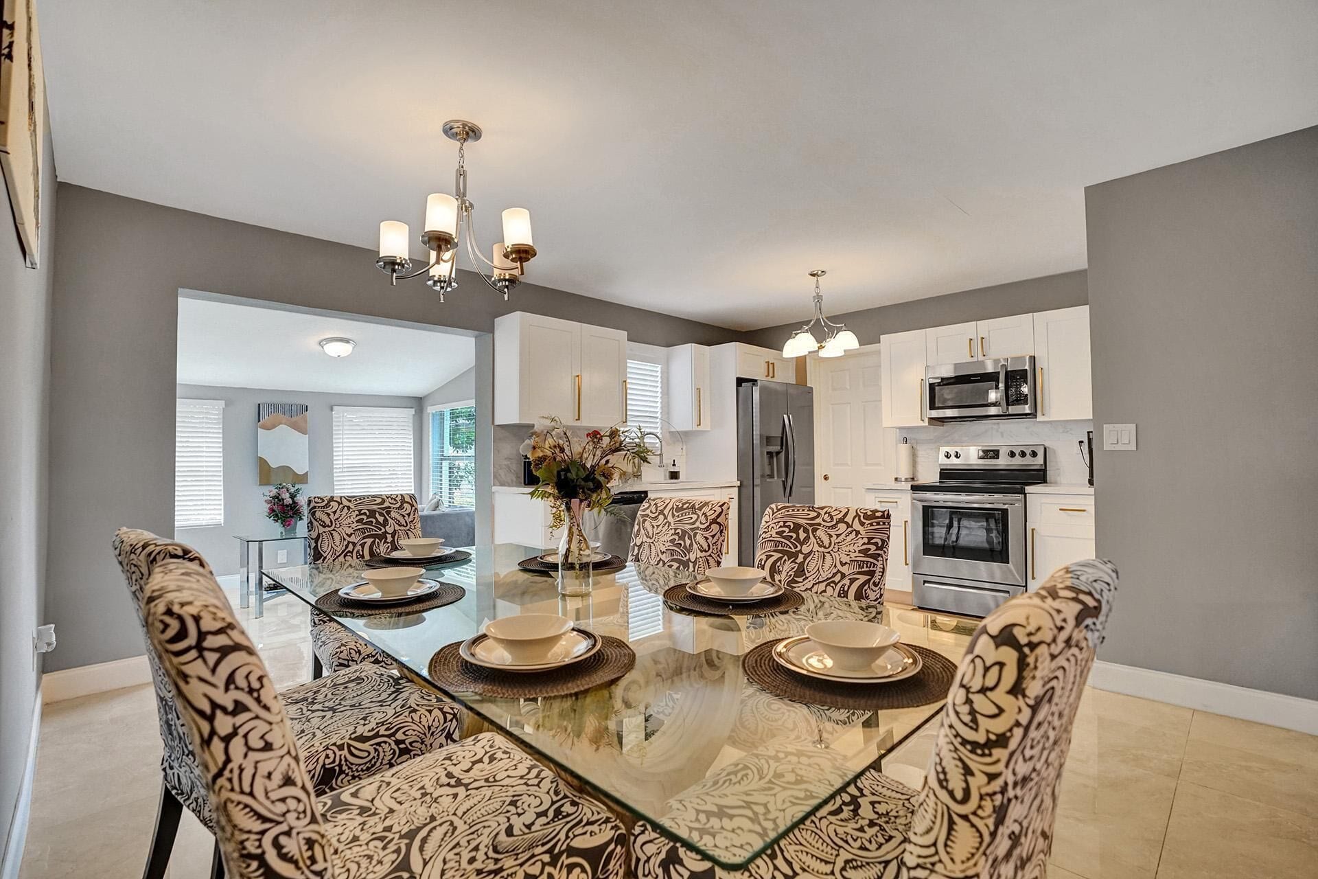 A modern kitchen with white cabinets, stainless steel appliances, and a glass dining table with patterned chairs.