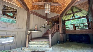 A wooden staircase leading to a second floor with a stone floor, a hanging lantern, and a view of greenery outside.