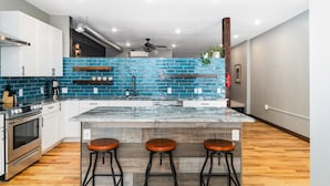 A modern kitchen with a blue backsplash, wooden shelves, a marble island, and three stools. - Craft District Loft - Michigan (Duluth)