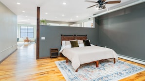 A modern bedroom with a large bed, a ceiling fan, and a view of a cityscape. - Craft District Loft - Michigan (Duluth)