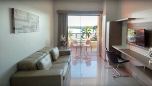 A modern living room with a sofa, a dining area, a TV, and a balcony with a view of the sea. - MARINA FLAT - ACHEI FÉRIAS (Caldas Novas)