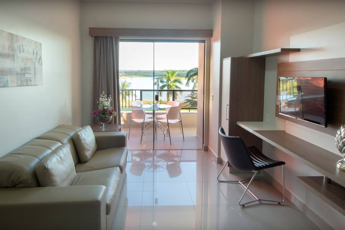 Una sala de estar moderna con sofá, comedor, televisor y balcón con vistas al mar.