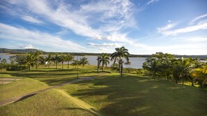 A golf course with a lake, palm trees, and a clear sky. - MARINA FLAT - ACHEI FÉRIAS (Caldas Novas)