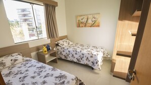 A hotel room with two beds, a window with curtains, a painting on the wall, and a wooden door. - MARINA FLAT - ACHEI FÉRIAS (Caldas Novas)