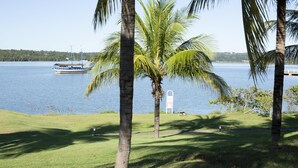 A grassy area with palm trees and a body of water in the background. - MARINA FLAT - ACHEI FÉRIAS (Caldas Novas)