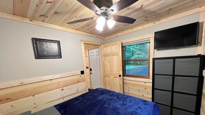 A bedroom with a bed, a ceiling fan, a TV, and a window with a view of trees. - The Morgan-Your Northwoods Escape! (Hayward)