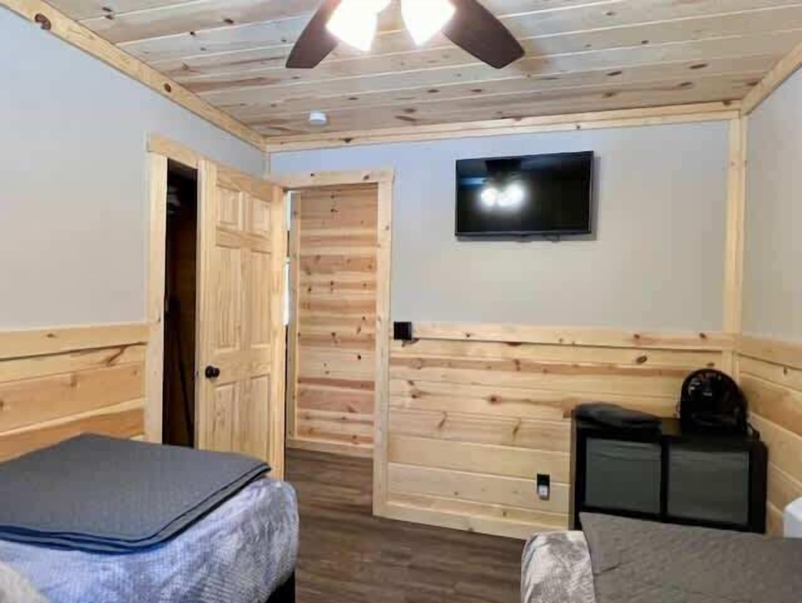 Una habitación con paneles de madera, una cama, una mesita y un televisor en la pared.