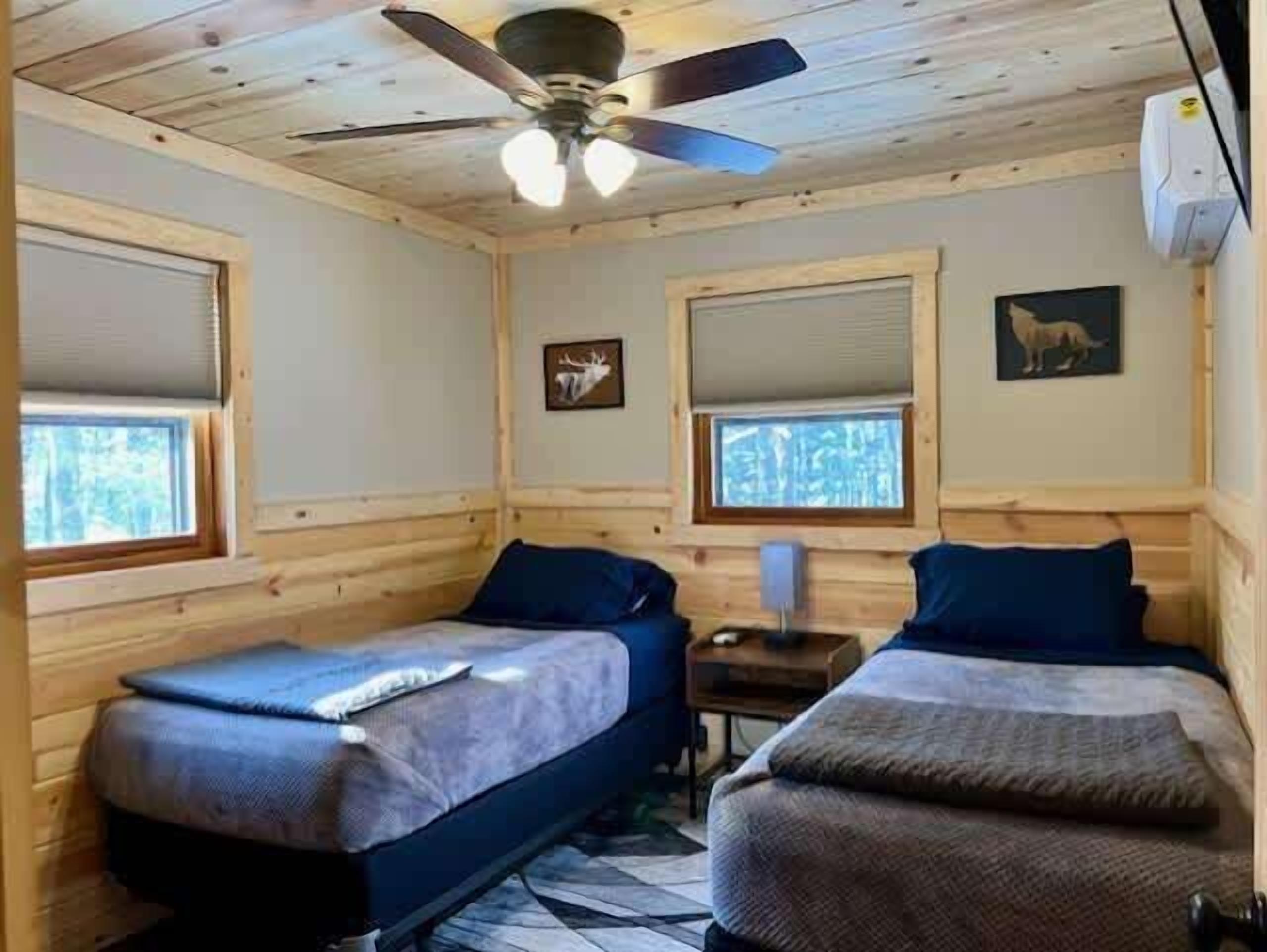 A cabin with two single beds, a ceiling fan, and a window with a forest view.