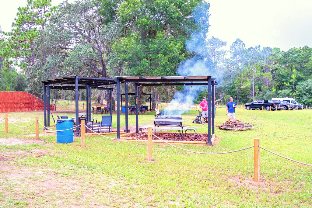 An outdoor area with a barbecue grill, picnic tables, and a covered seating area.