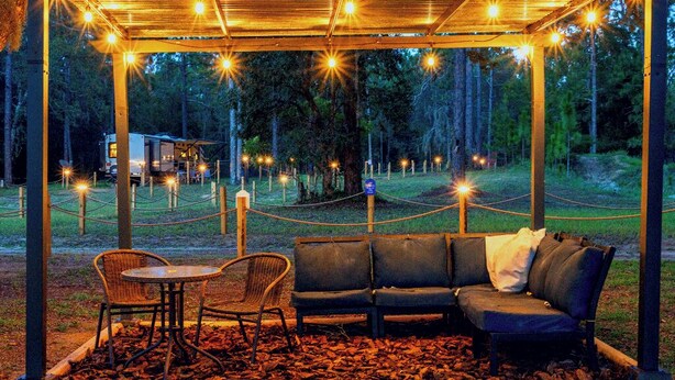 A covered seating area with a bench and chairs, surrounded by a rope barrier, and string lights overhead. - Fuel Your Passion for Epic Experiences and Outdoor Adventures at the Moto Ranch ATV! (Brooksville)