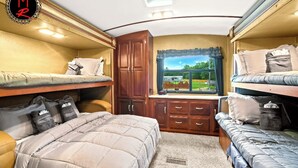A compact RV interior with bunk beds, a small kitchenette, and a window with a view of a house. - Fuel Your Passion for Epic Experiences and Outdoor Adventures at the Moto Ranch ATV! (Brooksville)