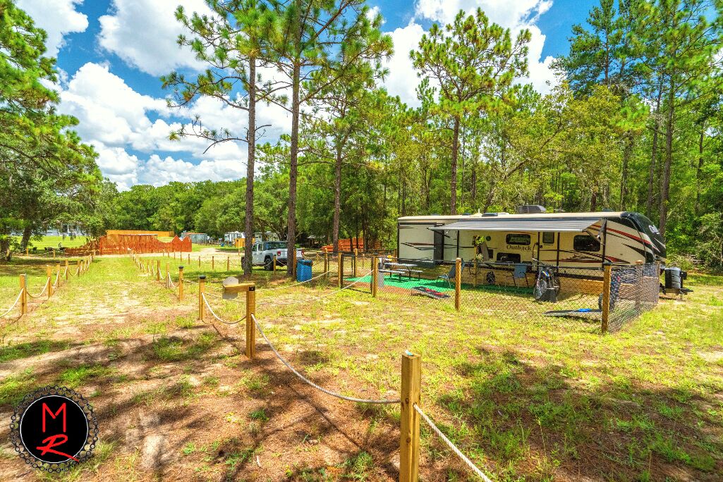 A recreational vehicle (RV) park with a large RV, fenced areas, and a lake in the background.