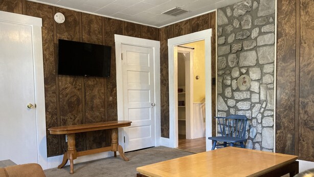 A living room with a wooden table, a blue chair, a brown couch, and a stone wall.