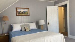 A bedroom with a bed, two bedside tables, a nightstand, a lamp, a door, and a framed picture on the wall.