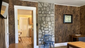 A room with a stone wall, wooden paneling, a wooden bench, a blue chair, and a small table.