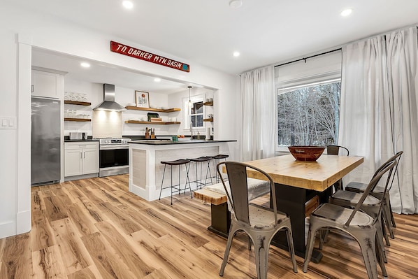 Una cocina moderna con armarios blancos, una mesa de comedor de madera y taburetes de bar.