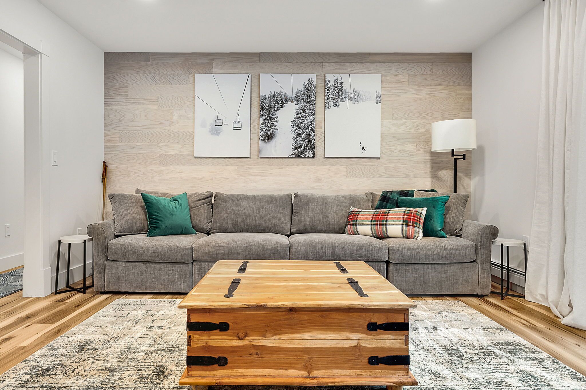 A modern living room with a grey sofa, a wooden coffee table, and three wall-mounted artworks depicting winter scenes.