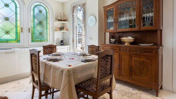 Una sala da pranzo con un tavolo imbandito per quattro persone, un mobiletto in legno con vetrate e una finestra con vetro verde.