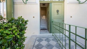Una scala conduce a una porta con cornice verde, ringhiera verde e un arco decorativo sopra.