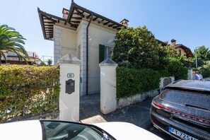 A building with a gated entrance, a car parked in front, and a person walking nearby.