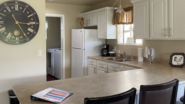 A kitchen with white cabinets, a central island with two chairs, a clock on the wall, and recessed ceiling lights. - NO STAIRS!  Walk-in condo, Golf Course View, No pets allowed.  (Branson)
