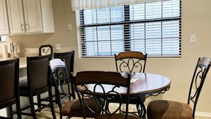 A dining area with a round table, six chairs, and a window with blinds. - NO STAIRS!  Walk-in condo, Golf Course View, No pets allowed.  (Branson)