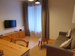 Ett kompakt vardagsrum med en platt-TV, trämöbler, ett litet bord och en soffa.