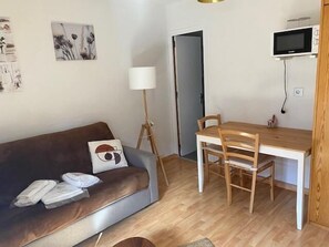 Una sala de estar con un sofá marrón, una mesa de comedor de madera con sillas, una lámpara de pie y un televisor montado en la pared.
