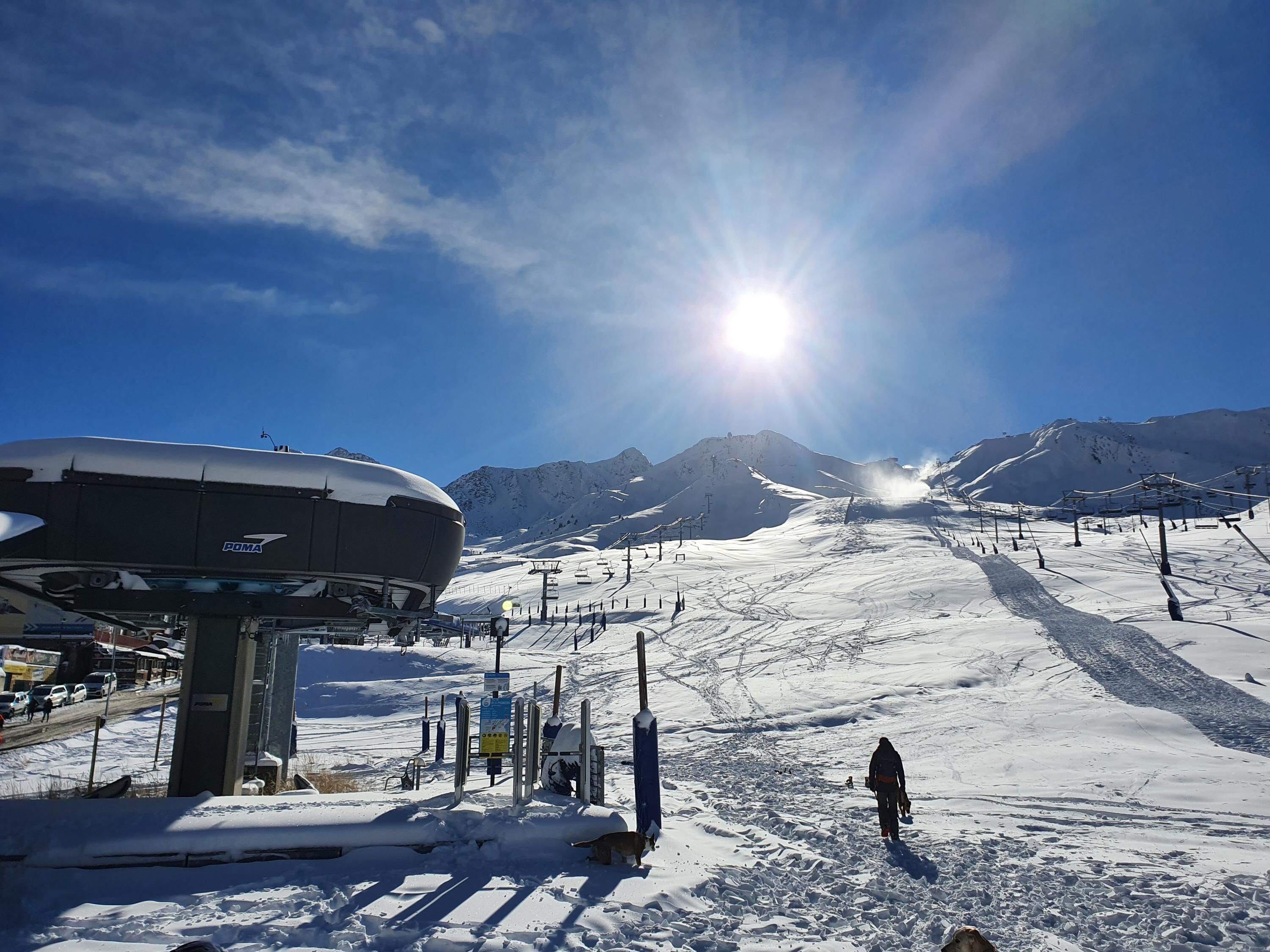 A ski resort with a large snow-covered mountain in the background, a ski lift, and a person skiing down the slope.