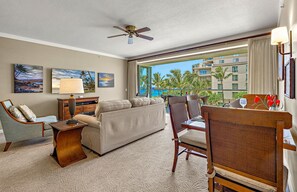 A hotel room with a balcony, a ceiling fan, a sofa, a chair, a table, and artwork on the walls.