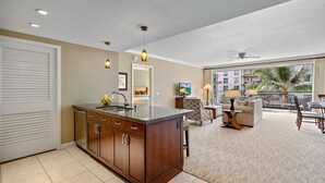Een moderne hotelkamer met een keukenhoek, een zithoek met een bank en een eettafel, en een balkon met uitzicht op de stad.
