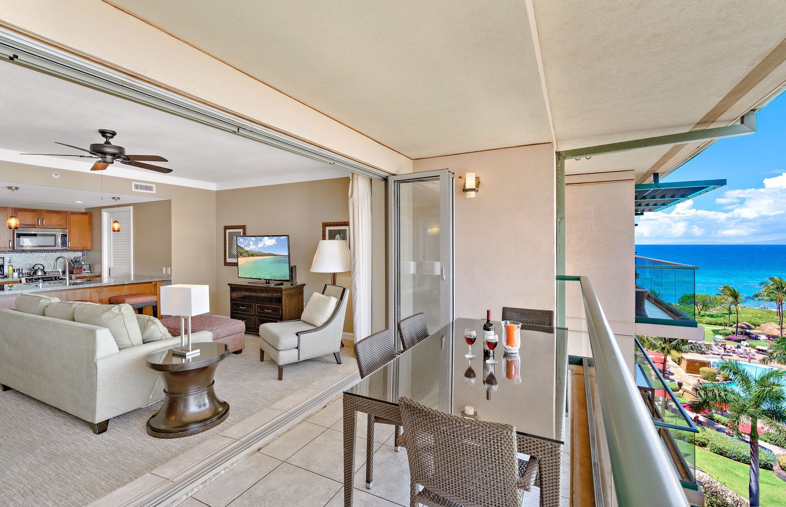 A balcony with a view of the ocean, a dining area with a table and chairs, a sofa, and a television in the living room.