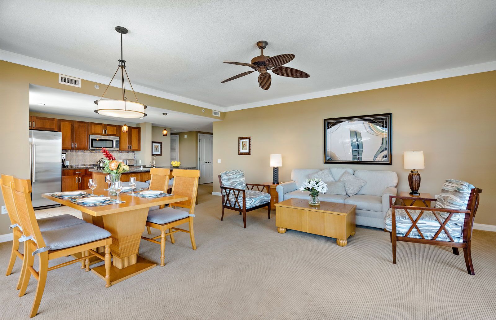 A modern living room with a dining area, a ceiling fan, and a kitchen in the background.