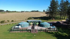 A yurt-style accommodation with a central entrance, a covered outdoor seating area, and a fenced perimeter.