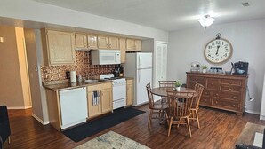 A compact kitchen with wooden cabinets, a microwave, a stove, and a dining area with a table and chairs. - 1 BR Walk in! No Cleaning Fees! Pools/hot tub! WAFFLES! Beach Pass! (Branson)