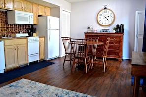 Une cuisine avec des meubles de rangement en bois, un four à micro-ondes, un réfrigérateur, une table à manger avec des chaises et une horloge murale.