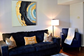 Un salon avec un canapé bleu foncé, une lampe et un tableau accroché au mur.
