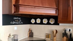A kitchen with a black countertop, wooden cabinets, and a black stove. There are wooden utensils and a salt shaker on the counter. - Charming 5-Bed House in Granja (Granja)