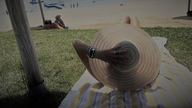 A person lying on a beach towel with a large hat, overlooking a beach with people and boats in the distance. - Charming 5-Bed House in Granja (Granja)