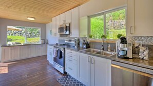 A modern kitchen with white cabinets, stainless steel appliances, a large window, and a wooden ceiling. - Waterfront Gig Harbor Home w/ Furnished Deck (Gig Harbor)