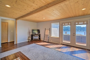 Un salón amplio con techo de madera, un televisor de pantalla plana, un ventanal con vista a un lago y una puerta corrediza de vidrio.
